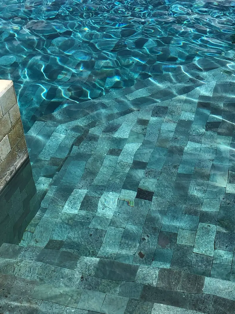 Losetas cuadradas de piedra verde bajo el agua, con reflejos de luz sobre el fondo de la piscina